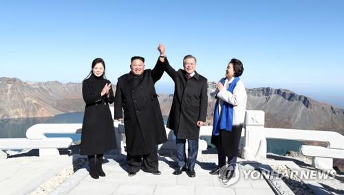 South Korean President Moon Jae-in (2nd from R) and North Korean leader Kim Jong-un raise each other's hand atop the North's Mount Paekdu on Sept. 20, 2018, as their wives, South Korean first lady Kim Jung-sook (R) and her North Korean counterpart Ri Sol-ju, applaud. (Yonhap)