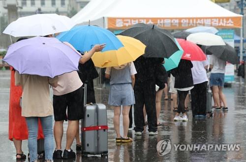 People carrying umbrellas stand in line for COVID-19 tests at a makeshift testing station at Seoul Plaza in central Seoul on July 31, 2022, as the country has experienced a new virus wave. (Yonhap)