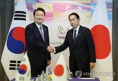 South Korean President Yoon Suk Yeol (L) and Japanese Prime Minister Fumio Kishida shake hands during a summit in Hiroshima, Japan, on May 21, 2023. (Yonhap)