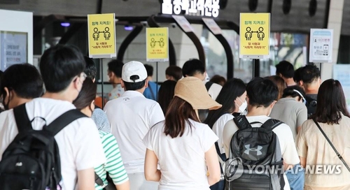 Des touristes font la queue avec des pancartes demandant la distanciation sociale en arrière-plan, à l'aéroport international de Gimpo le vendredi 30 juillet 2021.