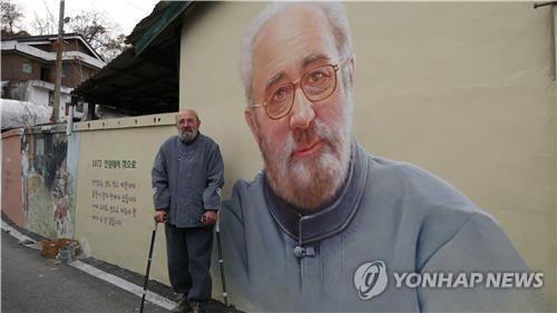 L'abbé Ji Jung-hwan devant un mur où est peint son portrait. (Photo fournie par le comté d'Imsil. Revente et archivage interdits)