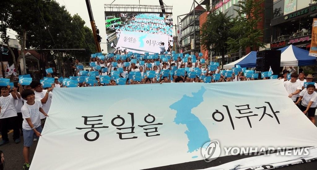 ２０１５年８月にソウルで開かれた民間団体主催の「民族統一大会」で、「統一を成し遂げよう」と書かれた横断幕を手にする参加者（資料写真）＝（聯合ニュース）