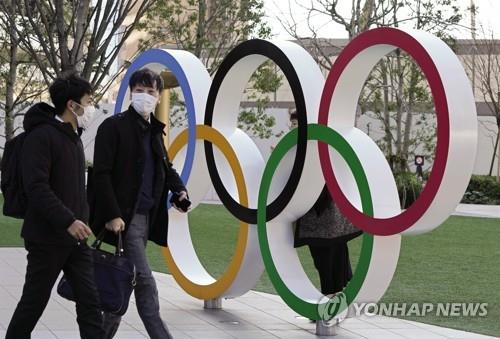 27일(현지시간) 올림픽 상징물 앞을 마스크를 쓴 일본 시민들이 지나가고 있다.