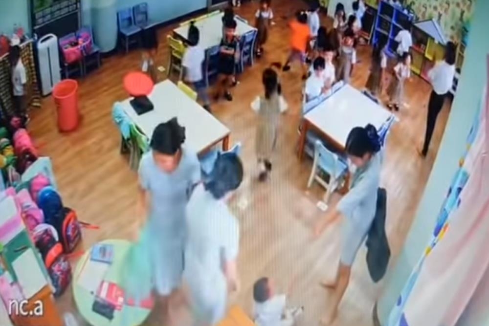보육교사 한 명이 바닥의 아동에게 검은 쓰레기봉투로 위협하는 모습.