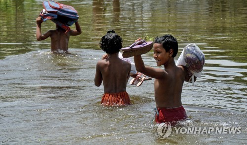 19일 방글라데시 가이반다 지역에서 어린이들이 신발 등을 손에 들고 물을 건너고 있다.[AP=연합뉴스 자료사진]