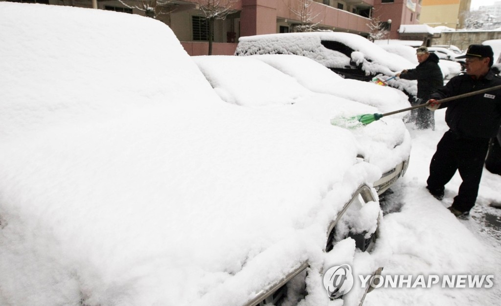 한 아파트 단지에서 경비원들이 차 위에 쌓인 눈을 치우고 있다. (연합뉴스 자료사진)