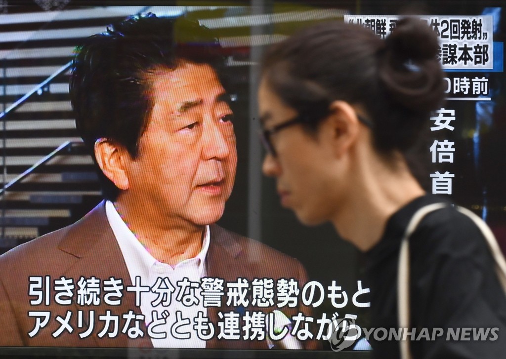 지난 16일 일본 도쿄 거리에서 한 여성이 이날 북한의 발사체 발사 관련 기자회견을 하는 아베 신조(安倍晋三) 총리의 모습을 전하는 TV 화면 앞을 지나치고 있다. [AFP=연합뉴스 자료사진]