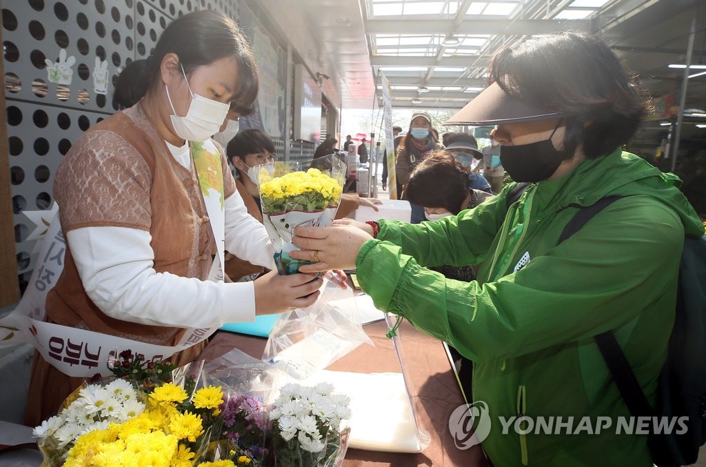 Workers distribute flowers to visitors during a campaign to promote social distancing at a market on the southern resort island of Jeju on Oct. 27, 2020. (Yonhap)