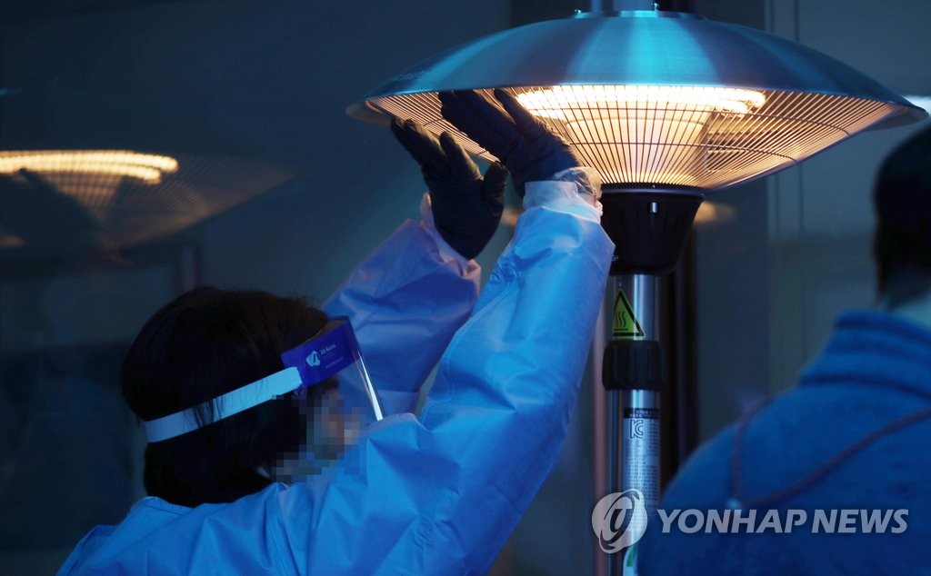A health official working in an outdoor screening station at the National Medical Center in Seoul warms up next to a heating device on Nov. 4, 2020. (Yonhap)