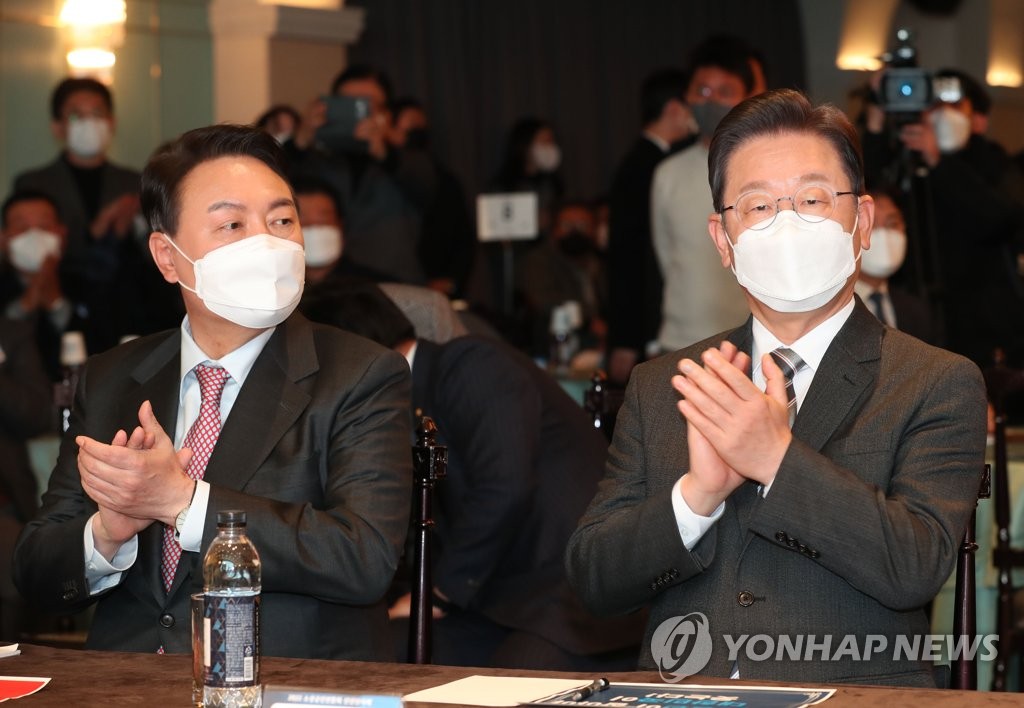 Yoon Suk-yeol (L), the presidential candidate of the main opposition People Power Party (PPP), and Lee Jae-myung, the presidential candidate of the ruling Democratic Party (DP), clap their hands during a event hosted by an association of small businesses in Seoul on Jan. 18, 2022. (Pool photo) (Yonhap)