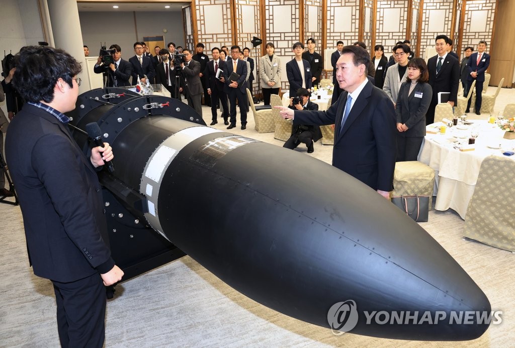 El presidente de Corea del Sur, Yoon Suk Yeol (dcha.), observa un proyectil, el 21 de febrero de 2023, en la oficina presidencial, en Seúl, antes de sostener un almuerzo de trabajo con un grupo de personas dedicadas a los esfuerzos del país para abrir camino en la industria espacial.
