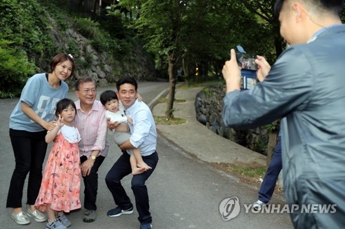 President Moon Jae-in (3rd from L) bends his knees to take a photo with a family at his personal residence in Yangsan, South Gyeongsang Province, on May 21, 2017. (Yonhap)