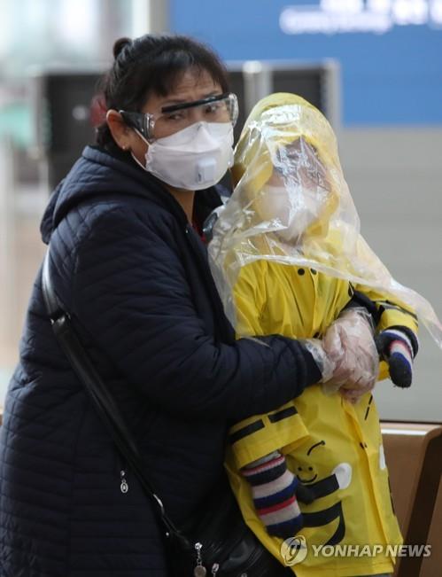 A Chinese mother wearing goggles and a mask and clutching her raincoat-clad child waits in the departure lounge of Incheon airport, west of Seoul, on March 4, 2020, amid concern about the spread of the new coronavirus. (Yonhap)