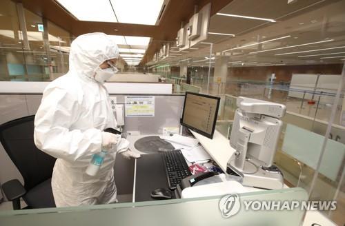 An immigration official clad in protective gear disinfects his desk at an immigration stand exclusively for inbound visitors with symptoms of the new coronavirus at Incheon airport, west of Seoul, on April 8, 2020. (Yonhap)
