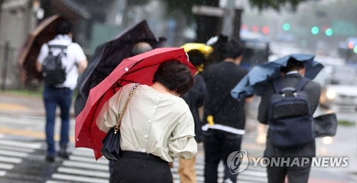 This file photo shows citizens walking on a street amid rain and strong wind. (Yonhap)