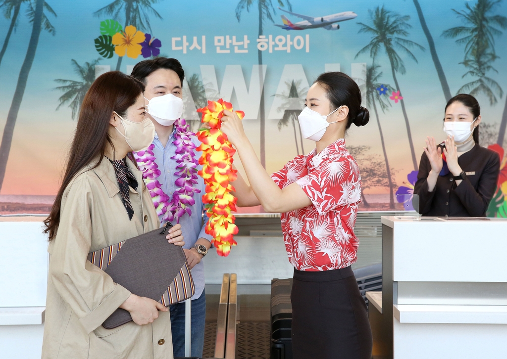 In this photo taken April 3, 2022, and provided by Asiana Airlines Inc., an Asiana employee offers Hawaiian flower leis to newlyweds headed for Hawaii for their honeymoon at Incheon International Airport, west of Seoul. (PHOTO NOT FOR SALE) (Yonhap)