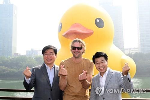 Dutch artist Florentijn Hofman (C) poses for a photo against the backdrop of the giant yellow rubber duck installation, along with Lotte Property & Development CEO Ryu Je-don (L) and Seo Gang-seok, head of Songpa Ward, in eastern Seoul on Sept. 29, 2022. (Yonhap)