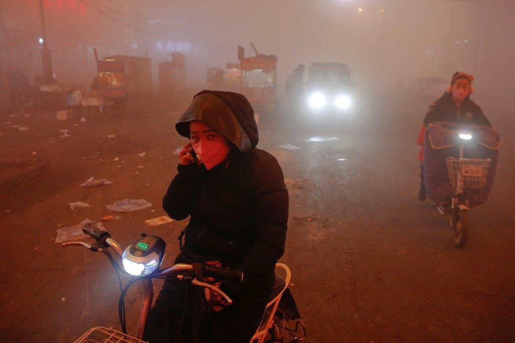 대기오염에 휩싸인 거리에서 자전거를 타고 가는 중국인들