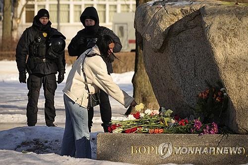 나발니를 추모하는 한 여성과 그를 지켜보는 경찰