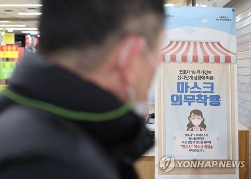El 18 de enero de 2023, una persona mira un cartel gubernamental que urge a los clientes el uso de mascarillas bajo techo, en un centro comercial de Seúl.