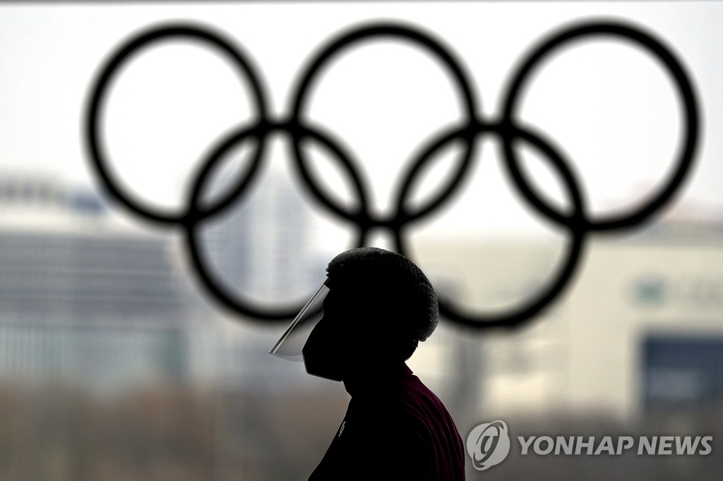 This Associated Press photo shows a person with a face shield walking past the Olympic Rings inside the Main Media Center for the 2022 Winter Olympics in Beijing on Jan. 19, 2022. (Yonhap)