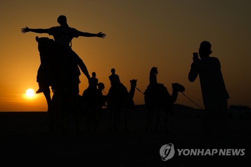 카타르 사막에서 낙타를 타고 기념 촬영을 하는 관광객들