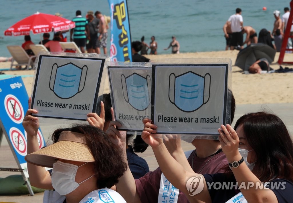 Officials at the southeastern port city of Busan hold signs in English asking visitors to wear masks at the city's Haeundae beach on July 5, 2020. (Yonhap)