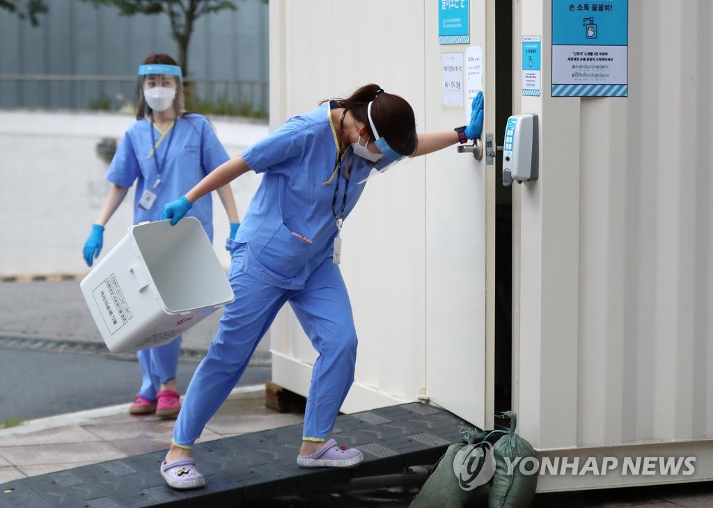 A health worker struggles to close a door at a screening center in eastern Seoul on Aug. 27, 2020, due to strong winds. (Yonhap)
