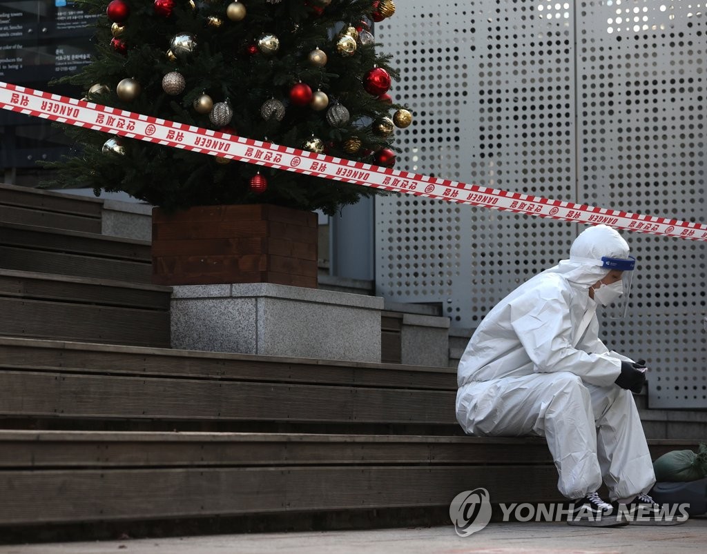 A medical worker takes a break below a Christmas tree near a COVID-19 screening station in Seoul on Dec. 24, 2020. (Yonhap) 