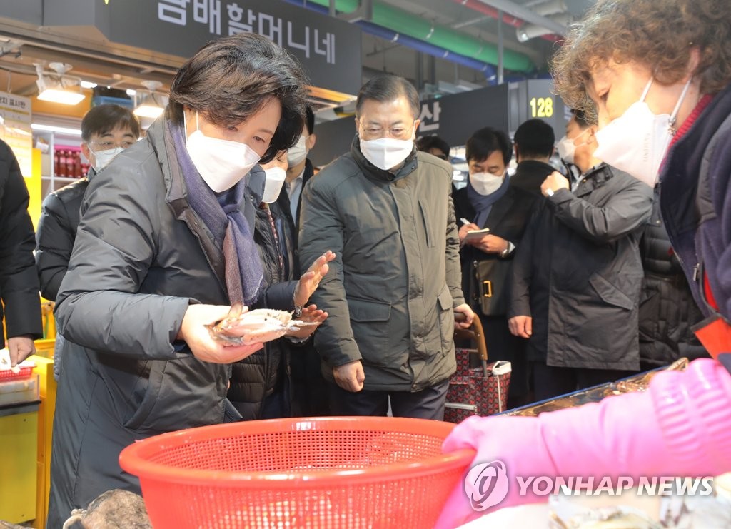 President Moon Jae-in (C) and first lady Kim Jung-sook (L) take a look at fishery products at the Soraepo-gu Fish Market in Incheon, 40 kilometers west of Seoul, on Feb. 10, 2021. Moon and Kim visited the market to hear out the hardships of small merchants going through tough times due to the new coronavirus and encourage them ahead of the Lunar New Year holiday. (Yonhap)
