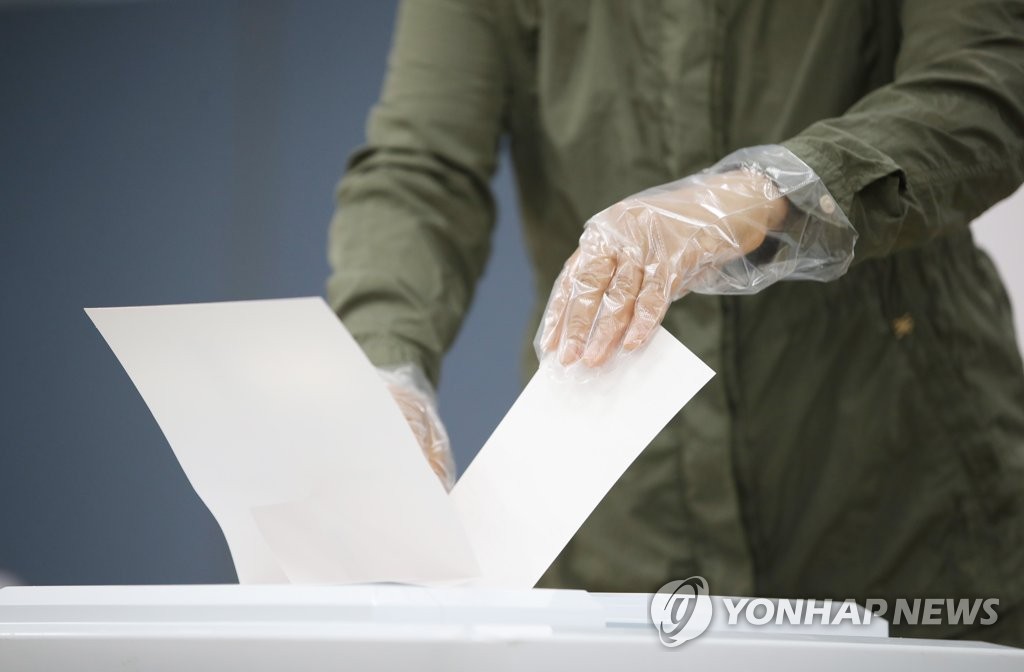 A voter wearing sanitary gloves places a vote in a ballot box for a mayoral by-election amid the coronavirus pandemic at a polling station in Seoul on April 7, 2021. (Yonhap)