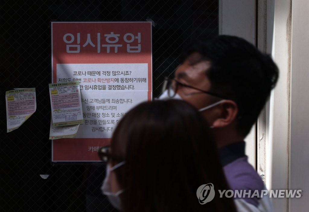People wearing masks pass by a cafe showing a closure notice in Seoul on Sept. 15, 2021. (Yonhap)
