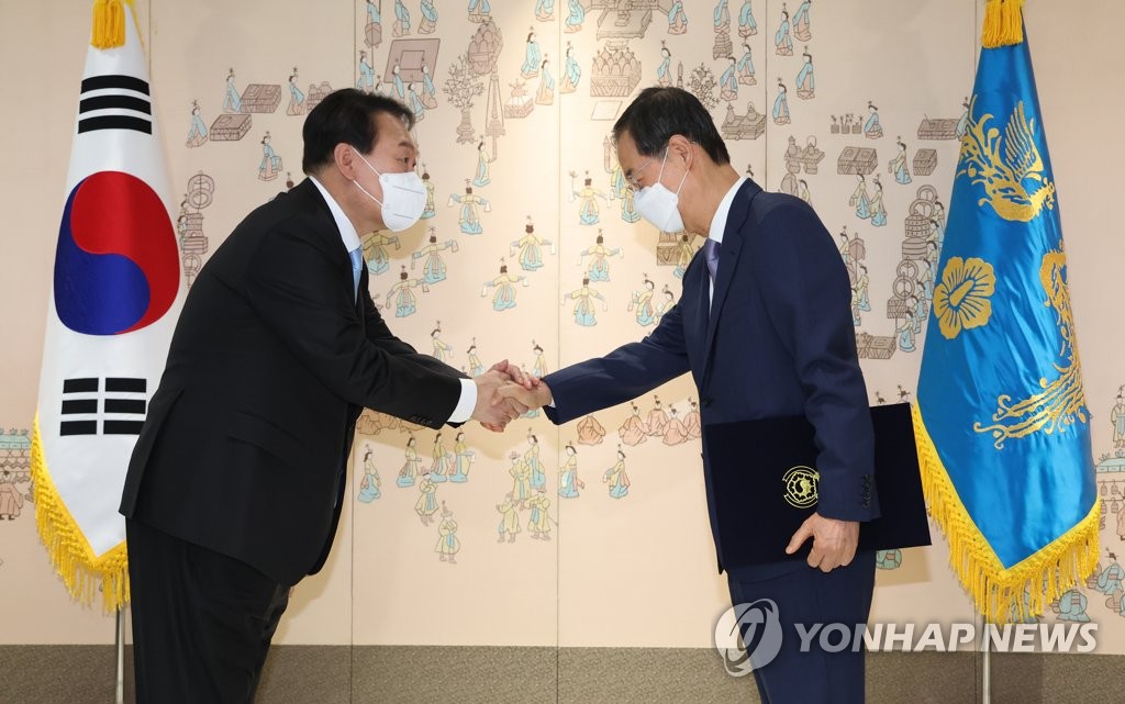 President Yoon Suk-yeol (L) shakes hands with Prime Minister Han Duck-soo after conferring an appointment certificate on Han at the presidential office in Seoul on May 21, 2022. (Yonhap)