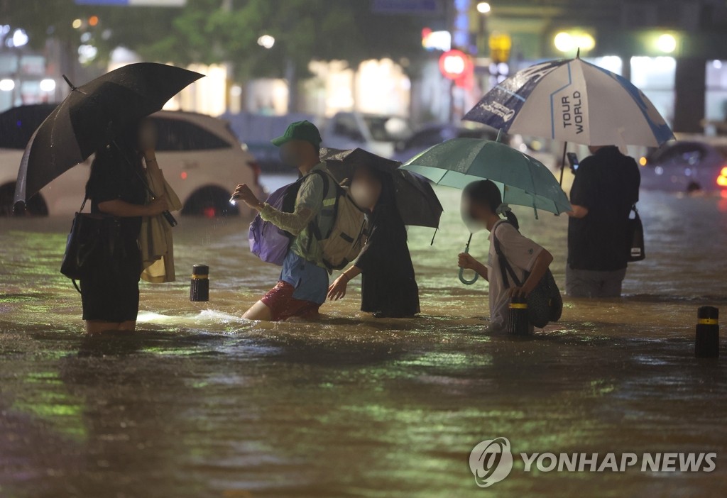 People wade though an inundated road in southern Seoul on the night of Aug. 8, 2022, as the heaviest rainfall of over 100 millimeters per hour in 80 years battered Seoul and surrounding areas. (Yonhap)