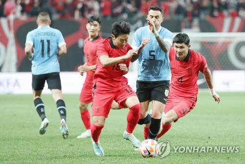 In this file photo from March 28, 2023, Lee Kang-in (L) and Kim Min-jae (R) of South Korea sandwich Matias Vecino of Uruguay during the teams' friendly football match at Seoul World Cup Stadium in Seoul. (Yonhap)