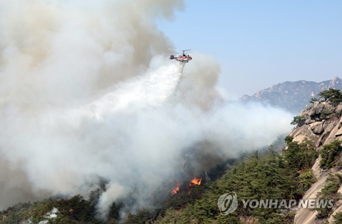 Un hélicoptère de l'Agence nationale contre les incendies (NFA) combat un incendie au mont Inwang à Jongno dans le centre de Séoul, le dimanche 2 avril 2023.